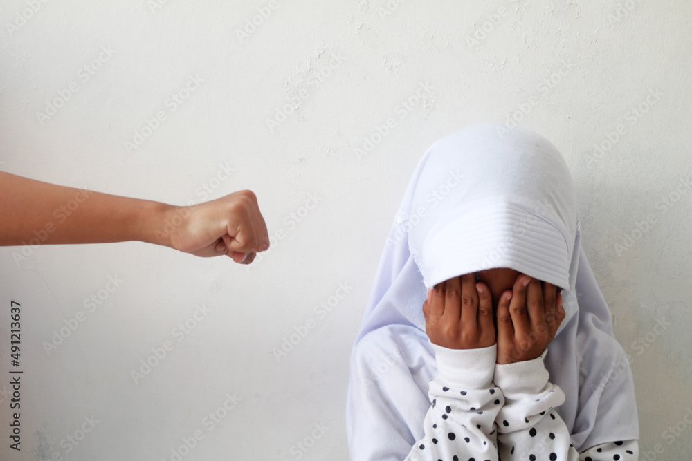Hands want to punch. Child with hijab covered his face with his hands