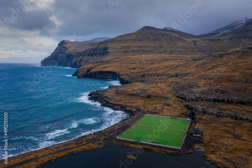 Aerial view of an old football field with scenic cliffs in the background located on the coast near the village of Eidi in Faroe Islands, Denmark. This football stadium is now used as a campsite