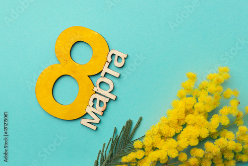 Greeting card for International Women's Day March 8. Blue background with a bouquet of mimosa flowers and the number eight from wood