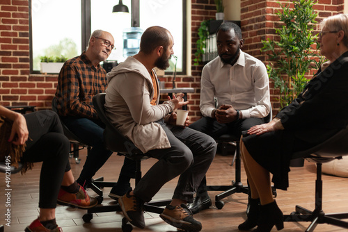 Multi ethnic group of people attending aa therapy meeting with psychologist. Patients with alcohol addiction having conversation about mental health problems while sitting in circle.