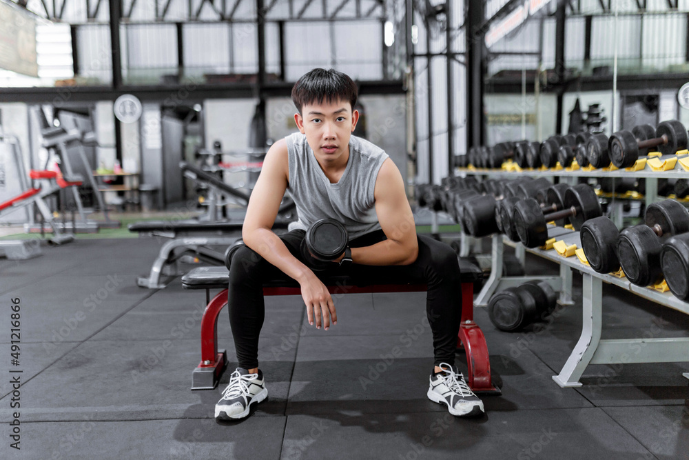 exercise concept The muscular guy in grey sport top and black pants and a black smartwatch working out with the dumbbell by doing concentration curl on his right arm exercise concept The muscular guy in grey sport top and black pants and a black smartwatch working out with the dumbbell by doing concentration curl on his right arm