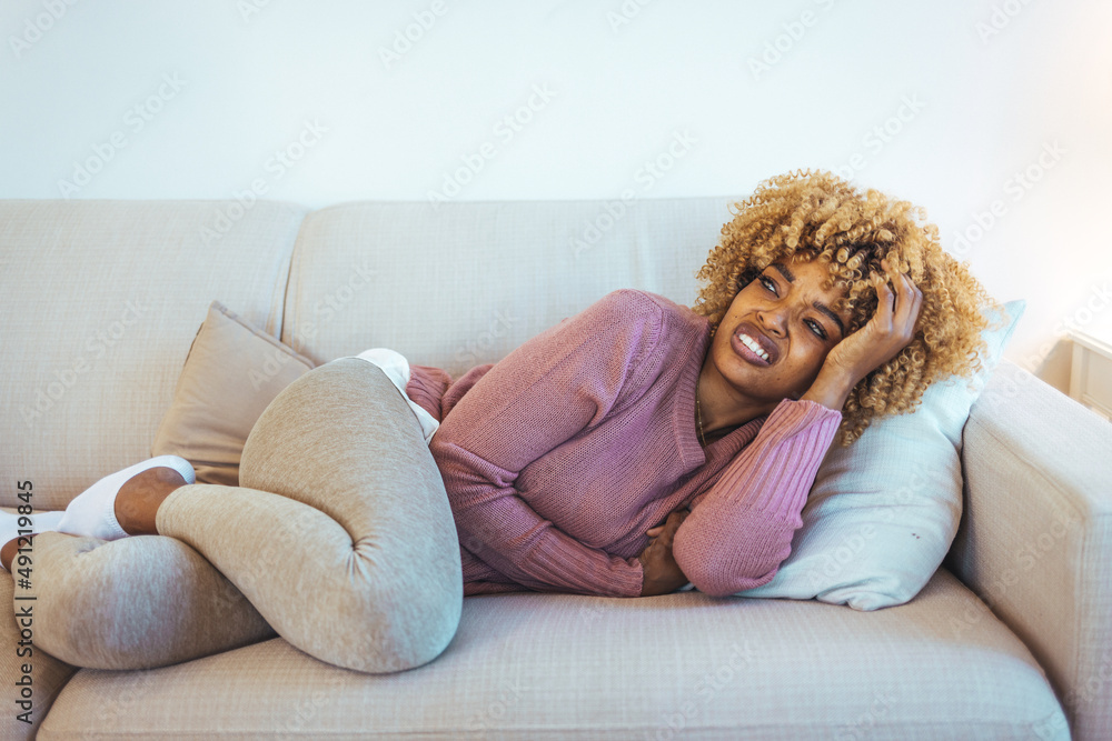 Cropped shot of an attractive young woman lying on her sofa alone and suffering from period cramps at home. Ouch! My tummy! Woman with menstrual pain. Woman with hands on stomach suffering from pain Cropped shot of an attractive young woman lying on her sofa alone and suffering from period cramps at home. Ouch! My tummy! Woman with menstrual pain. Woman with hands on stomach suffering from pain