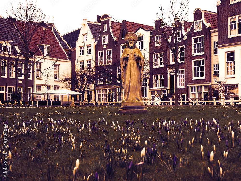Jesus statue surrounded by crocus flowers and historic houses in Begijnhof courtyard. Amsterdam, Netherlands. Easter time. Retro aged photo.