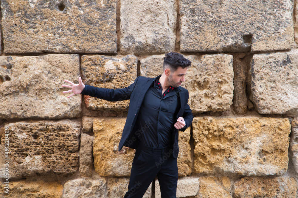 gypsy man dancing flamenco, young and handsome dressed in black and red shoes is posing and dancing on a background of a stone wall. Flamenco cultural heritage of humanity gypsy man dancing flamenco, young and handsome dressed in black and red shoes is posing and dancing on a background of a stone wall. Flamenco cultural heritage of humanity