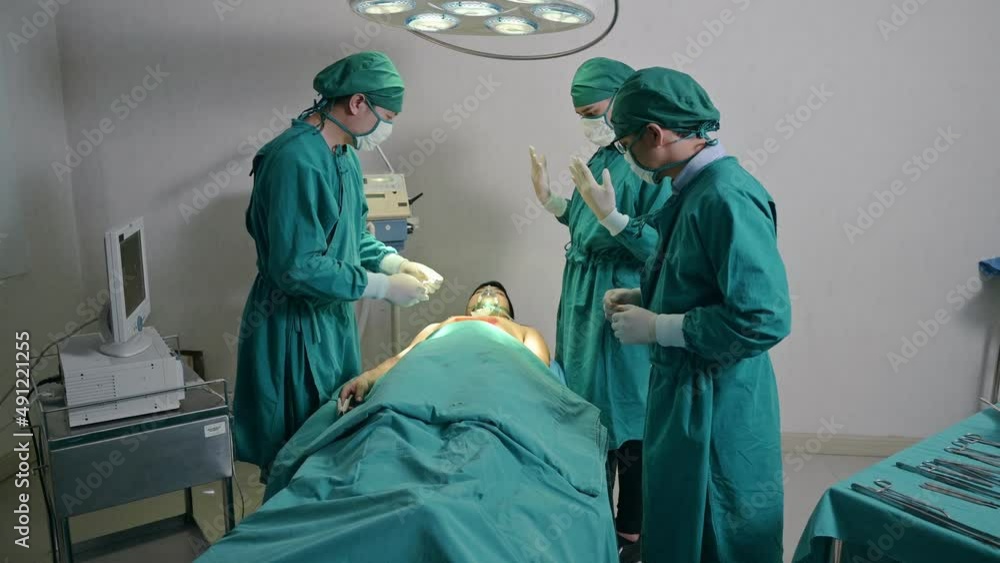 Surgeon team operating seriously injured patient with colleague picking up surgical equipment in hospital Surgeon team operating seriously injured patient with colleague picking up surgical equipment in hospital