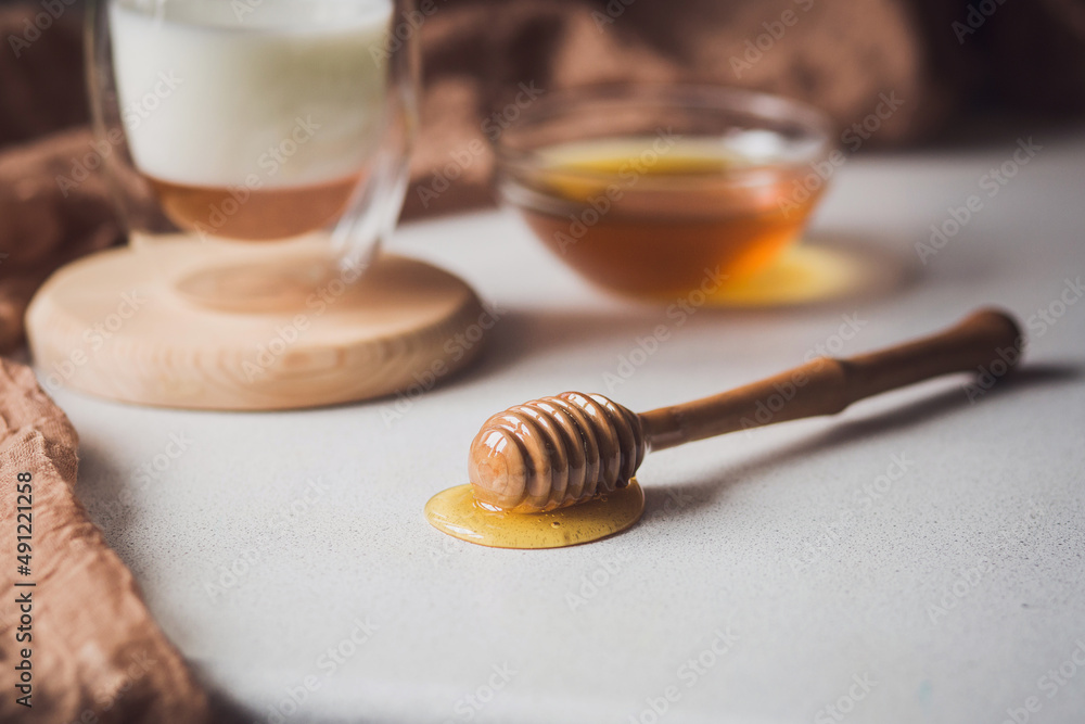 Milk and honey. Glass cup with milk and bowl with honey on the table. Spoon for honey. Breakfast, snack. Calming and healthy drink. Milk and honey. Glass cup with milk and bowl with honey on the table. Spoon for honey. Breakfast, snack. Calming and healthy drink.