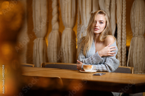 Portrait of a young beautiful woman sitting in modern cafe bar interior having a cup of coffee