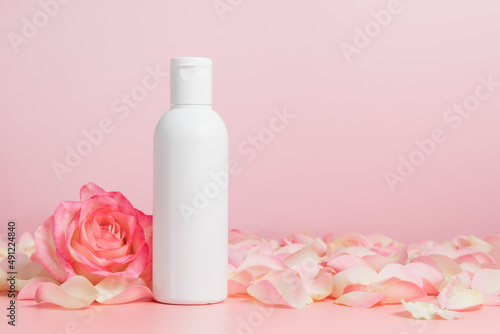 White unbranded mockup bottle of body lotion or shampoo with roses and petals, bottle for logo or design, natural cosmetic