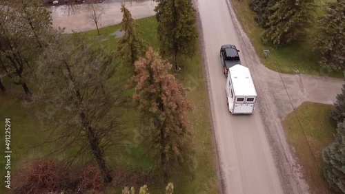 Black pick up truck towing horse trailer through small town, aerial follow view photo