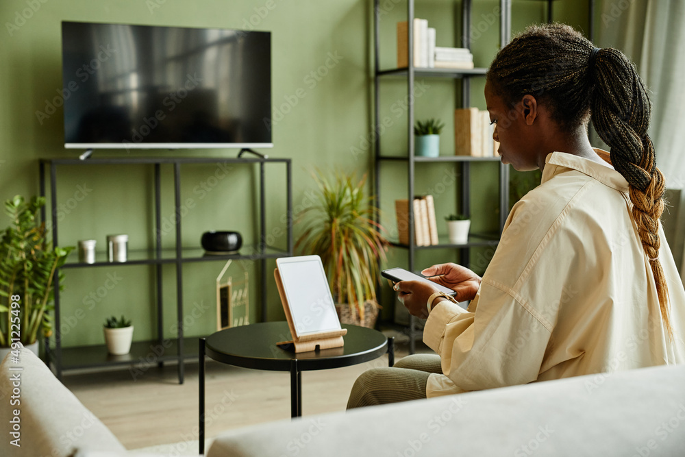 Side view portrait of young black woman connecting phone to smart home system with blank screen, copy space