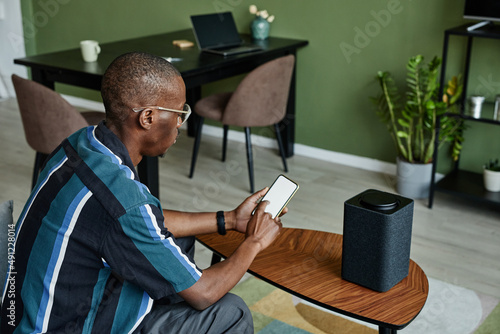 High angle view at modern black man connecting phone to smart speaker with voice controlled home AI photo