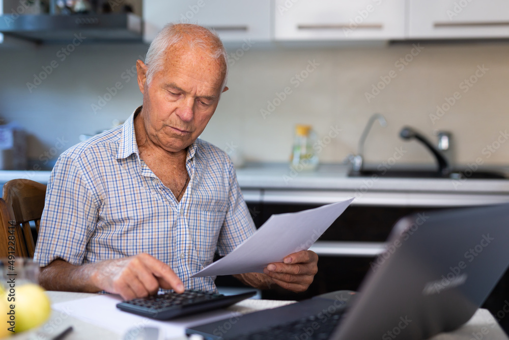 Old man sitting at table and counting with calculator Old man sitting at table and counting with calculator