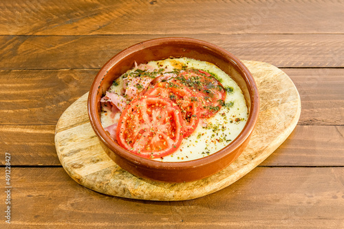 Great Italian recipe for a portion of grilled provolone cheese in a clay pot with tomato slices, cooked ham, a lot of oregano and some pesto sauce photo