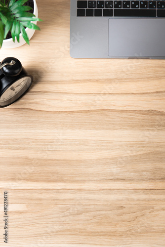 part of a desktop with a laptop, an alarm clock and a houseplant on an oak wooden background general view. Workspace on an oak table. top view. Flatley. Vertical