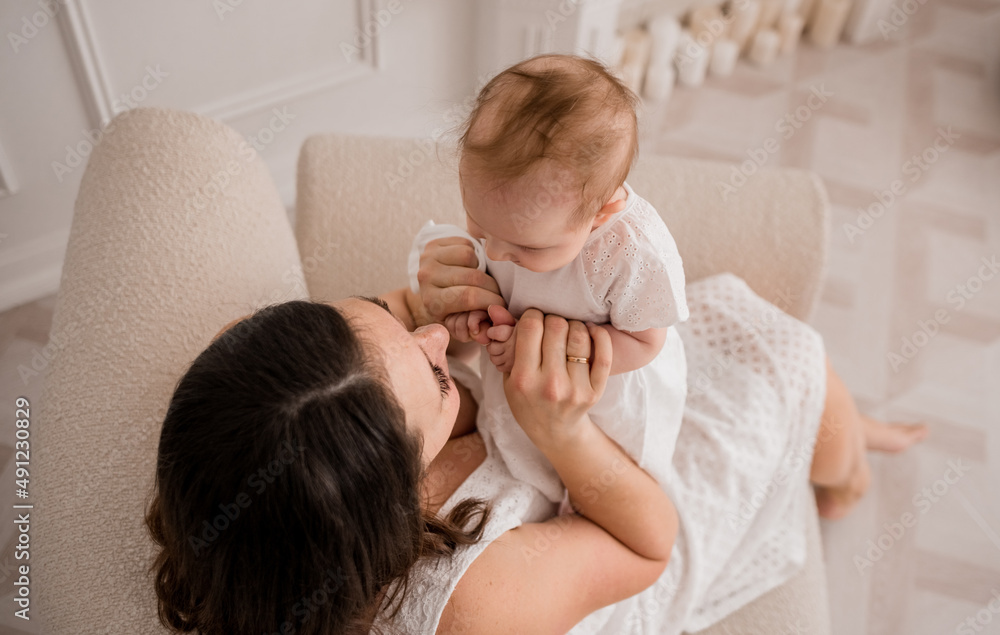 Caucasian brunette mom is sitting in a chair and playing with a baby girl Caucasian brunette mom is sitting in a chair and playing with a baby girl