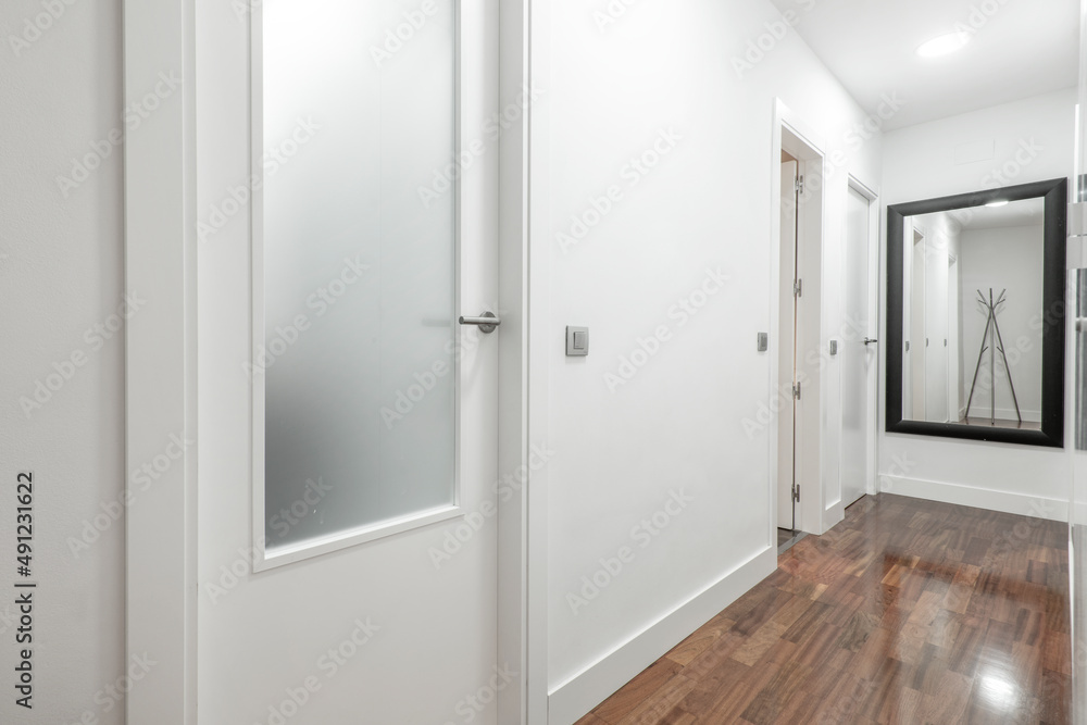 Hallway of a residential home with brown hardwood floors, pristine white walls, and a black-framed mirror Hallway of a residential home with brown hardwood floors, pristine white walls, and a black-framed mirror