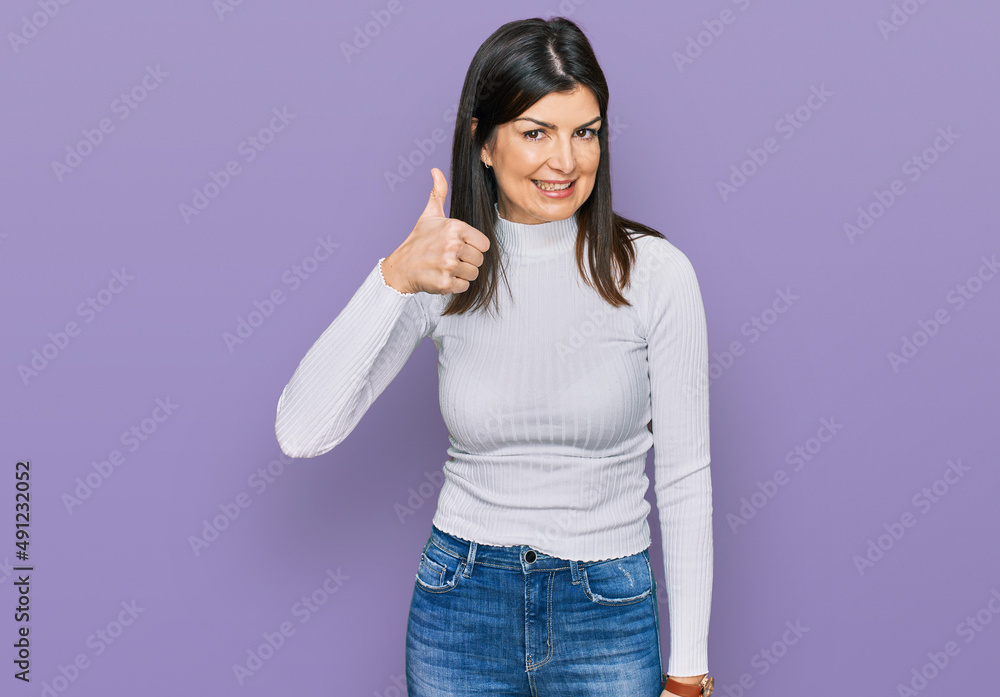 Beautiful brunette woman wearing casual clothes doing happy thumbs up gesture with hand. approving expression looking at the camera showing success. Beautiful brunette woman wearing casual clothes doing happy thumbs up gesture with hand. approving expression looking at the camera showing success.