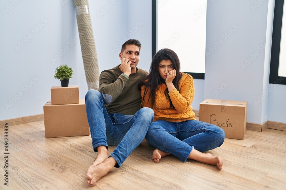 Young couple sitting on the floor at new home looking stressed and nervous with hands on mouth biting nails. anxiety problem. Young couple sitting on the floor at new home looking stressed and nervous with hands on mouth biting nails. anxiety problem.