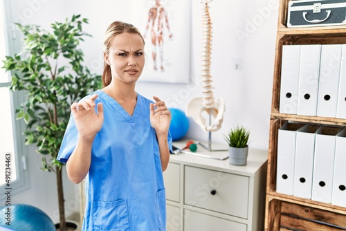 Young caucasian woman working at pain recovery clinic disgusted expression  displeased and fearful doing disgust face because aversion reaction. with hands raised