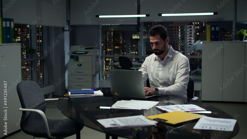 Successful entrepreneur work on laptop with night cityscape view outside panoramic windows. Successful entrepreneur work on laptop with night cityscape view outside panoramic windows.