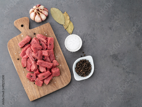 Chopped topside meat on wooden board over stone background with seasonings and copy space