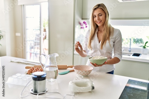 Young blonde woman smiling confident pouring flour on bowl at kitchen