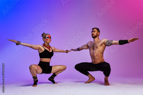 Beautiful young acrobats or gymnasts with colorful face painting on pink blue gradient background. Professional ballet couple dancing  Emotional duet performing choreographic art. Animal instinct