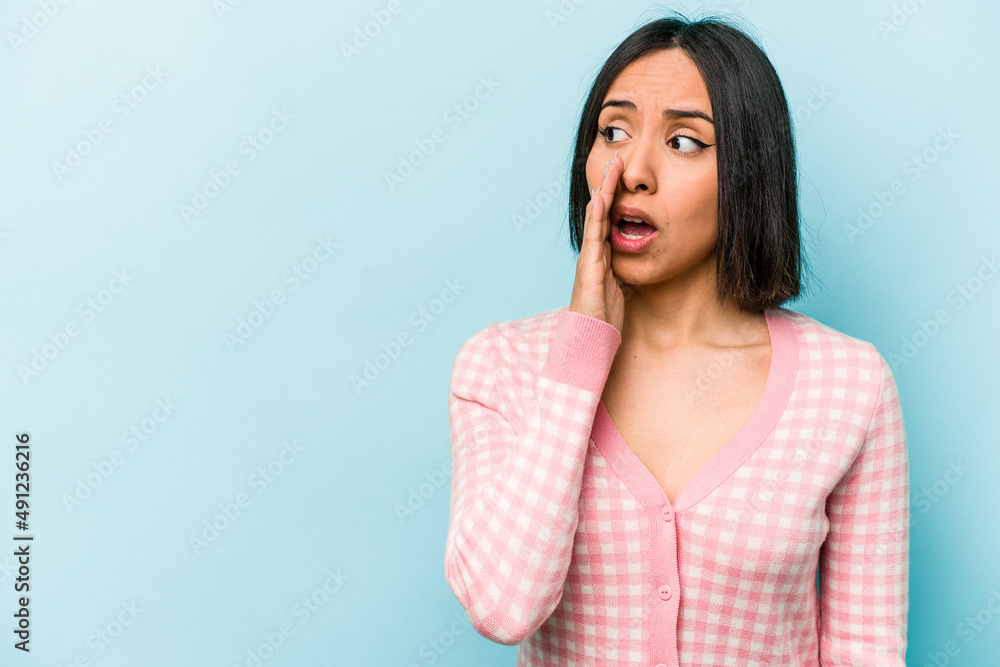 Young hispanic woman isolated on blue background is saying a secret hot braking news and looking aside Young hispanic woman isolated on blue background is saying a secret hot braking news and looking aside