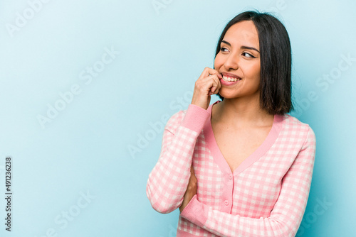 Young hispanic woman isolated on blue background relaxed thinking about something looking at a copy space.