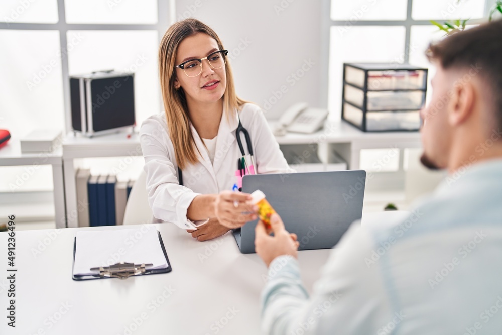 Young man and woman doctor and patient having medical consultation holding pills at clinic Young man and woman doctor and patient having medical consultation holding pills at clinic