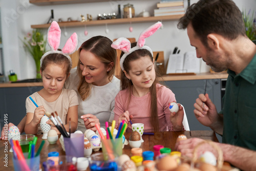 Cheerful caucasian family of four people decorates easter eggs in domestic kitchen