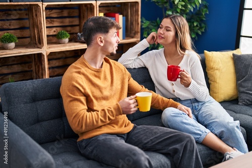 Young man and woman couple drinking coffee sitting on sofa at home