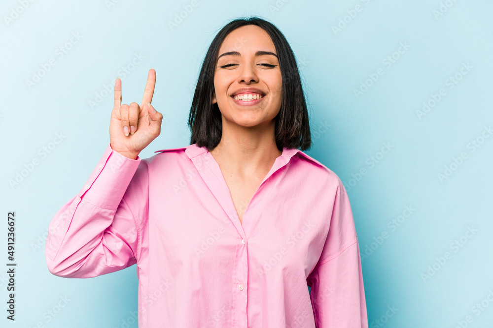 Young hispanic woman isolated on blue background showing a horns gesture as a revolution concept. Young hispanic woman isolated on blue background showing a horns gesture as a revolution concept.