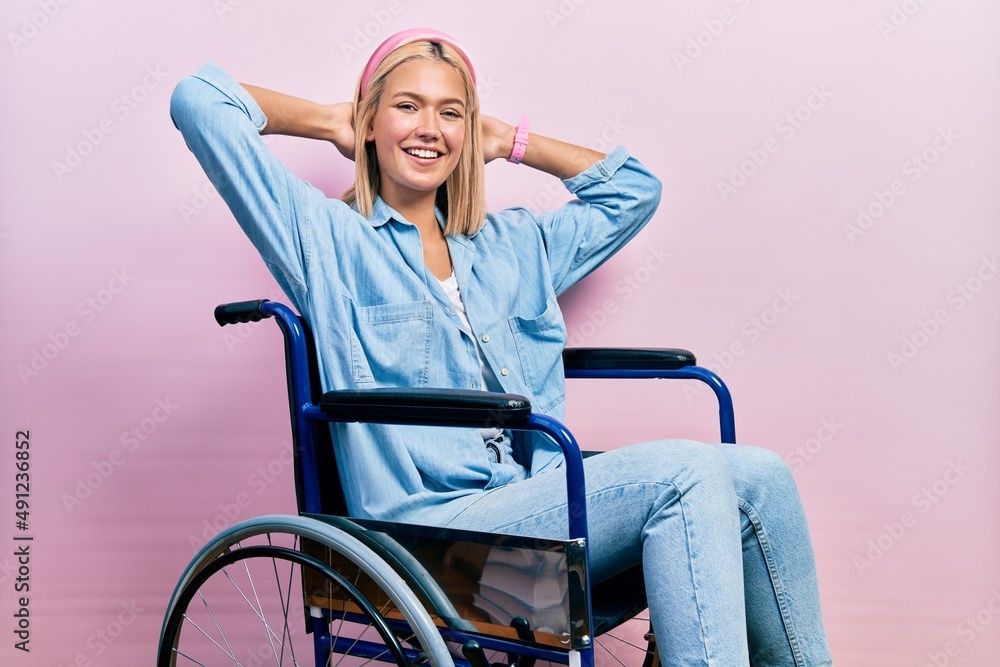 Beautiful blonde woman sitting on wheelchair relaxing and stretching, arms and hands behind head and neck smiling happy Beautiful blonde woman sitting on wheelchair relaxing and stretching, arms and hands behind head and neck smiling happy