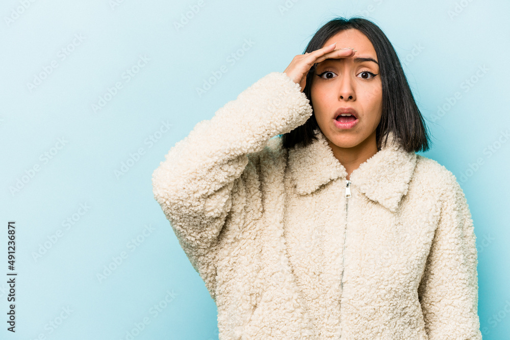 Young hispanic woman isolated on blue background looking far away keeping hand on forehead. Young hispanic woman isolated on blue background looking far away keeping hand on forehead.