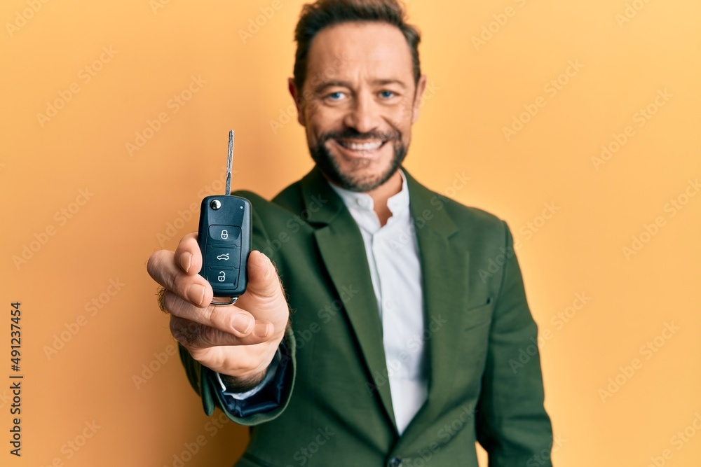 Middle age businessman holding key of new car looking positive and happy standing and smiling with a confident smile showing teeth Middle age businessman holding key of new car looking positive and happy standing and smiling with a confident smile showing teeth