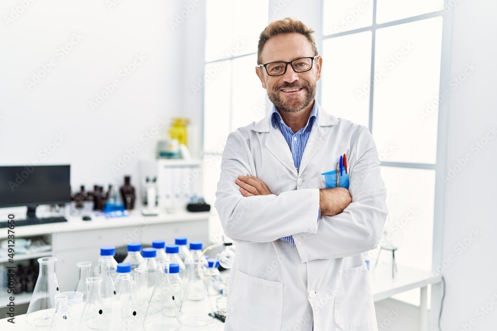 Middle age hispanic man wearing scientist uniform with arms crossed gesture at laboratory Middle age hispanic man wearing scientist uniform with arms crossed gesture at laboratory