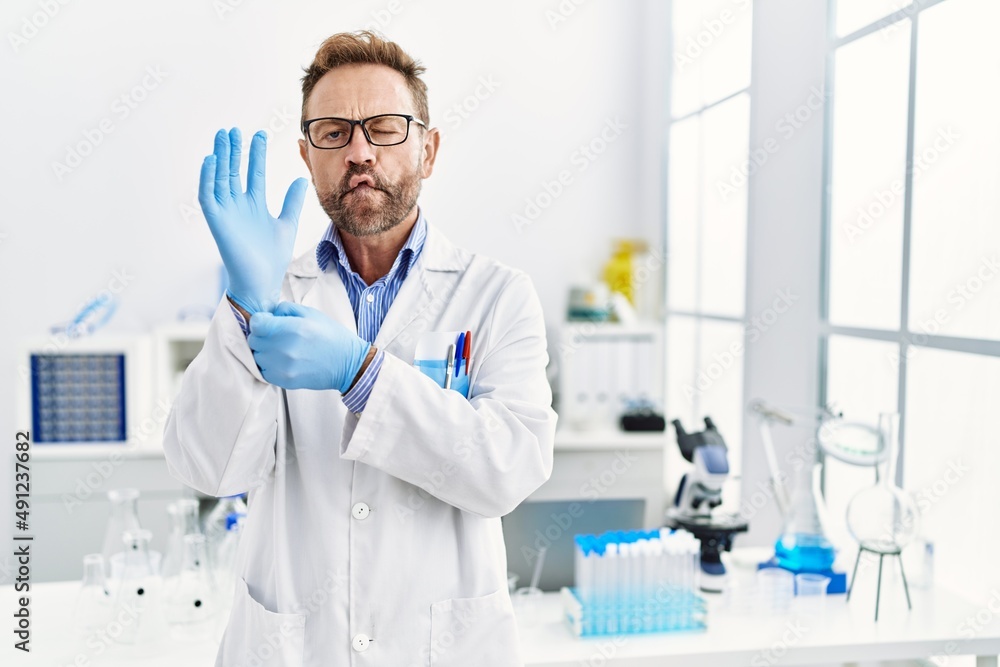 Middle age man working at scientist laboratory making fish face with mouth and squinting eyes, crazy and comical. Middle age man working at scientist laboratory making fish face with mouth and squinting eyes, crazy and comical.