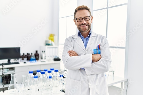 Middle age hispanic man wearing scientist uniform with arms crossed gesture at laboratory