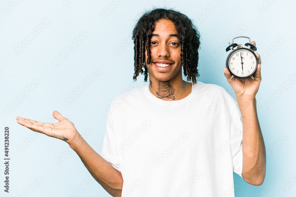 Young African american man holding alarm clock isolated on blue ...