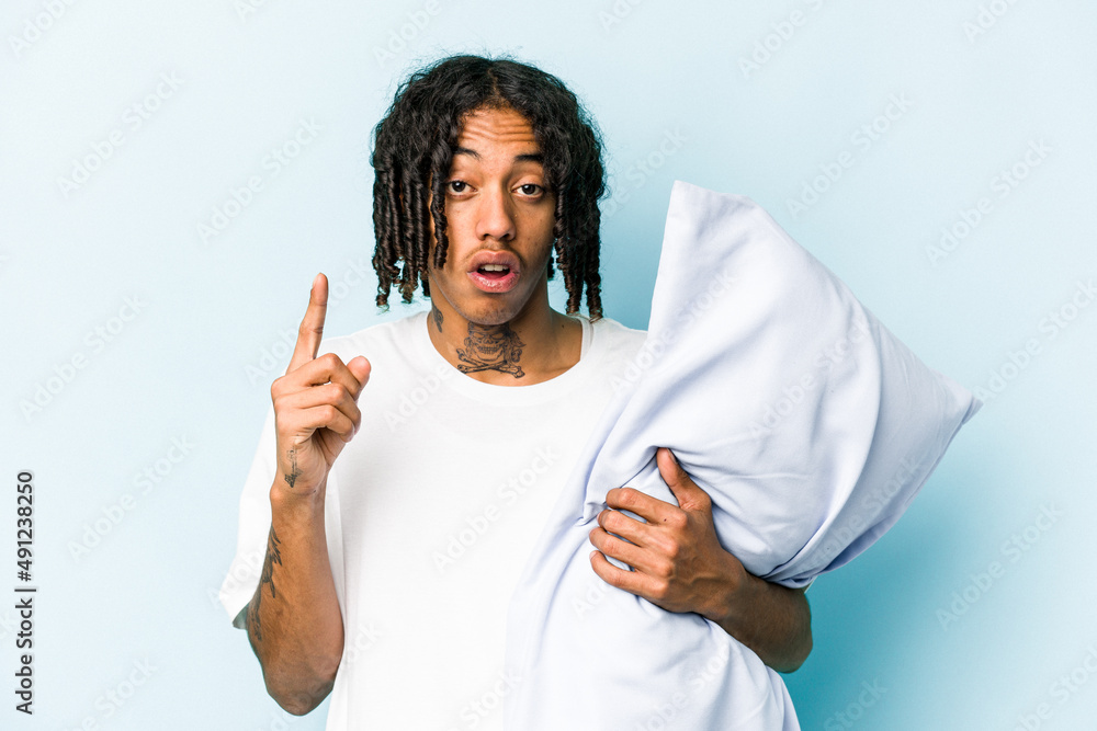 Young African American man holding a pillow isolated on blue background having some great idea, concept of creativity. Young African American man holding a pillow isolated on blue background having some great idea, concept of creativity.