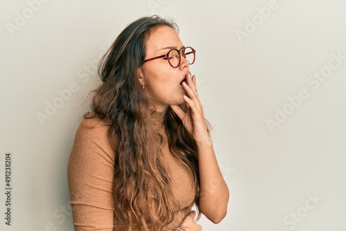 Young hispanic girl wearing casual clothes and glasses bored yawning tired covering mouth with hand. restless and sleepiness.