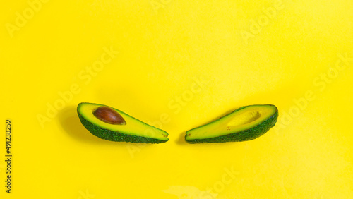 Two halves of a ripe avocado with a stone in the middle on a yellow background close-up.