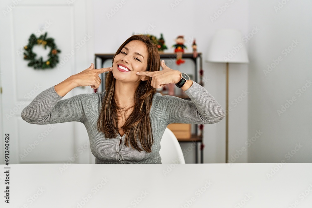 Φωτογραφία Young latin woman sitting on the table by christmas decor smiling cheerful showing and pointing with fingers teeth and mouth