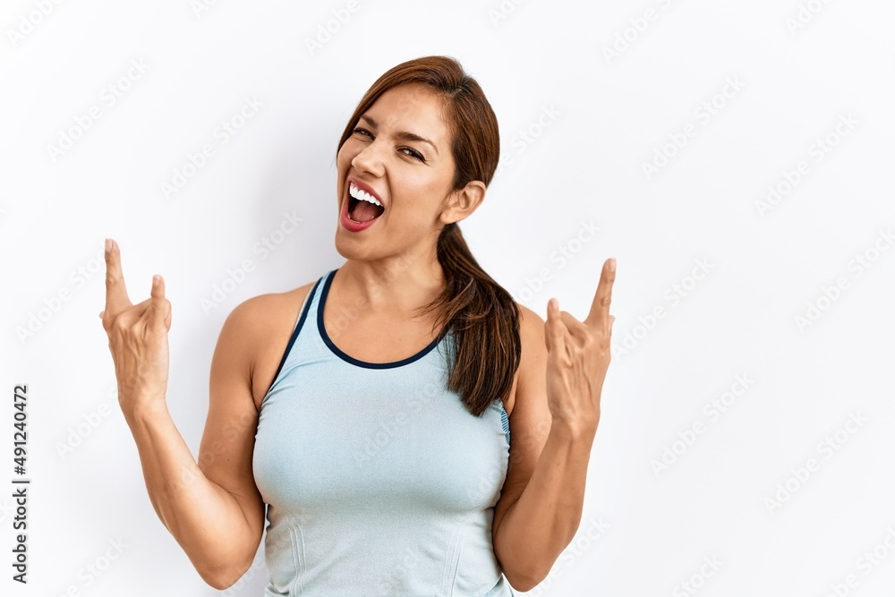 Young latin woman wearing sporty clothes over isolated background shouting with crazy expression doing rock symbol with hands up. music star. heavy concept. Young latin woman wearing sporty clothes over isolated background shouting with crazy expression doing rock symbol with hands up. music star. heavy concept.