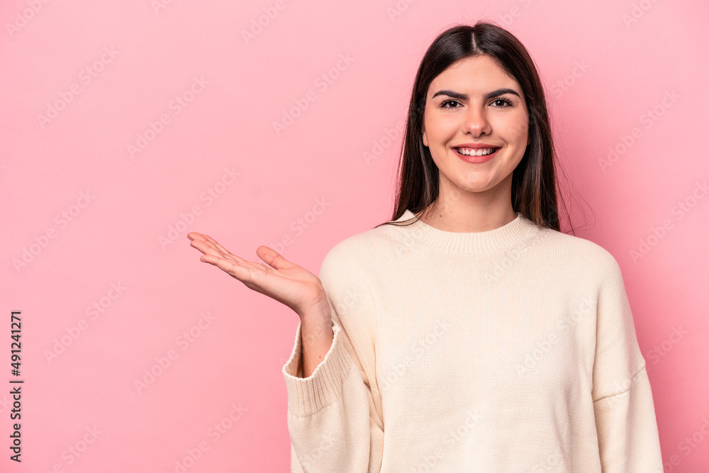 Young caucasian woman isolated on pink background showing a copy space on a palm and holding another hand on waist. Young caucasian woman isolated on pink background showing a copy space on a palm and holding another hand on waist.