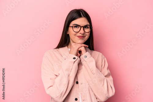 Young caucasian woman isolated on pink background keeps hands under chin, is looking happily aside. © Asier