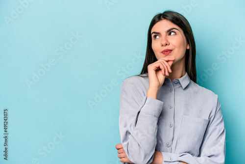 Young caucasian woman isolated on blue background relaxed thinking about something looking at a copy space.