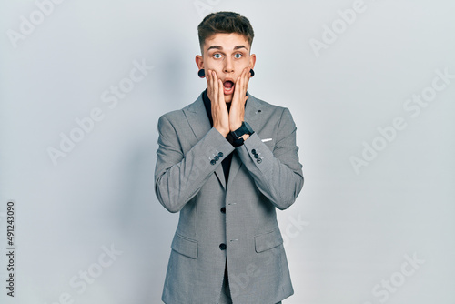 Young caucasian boy with ears dilation wearing business jacket afraid and shocked, surprise and amazed expression with hands on face