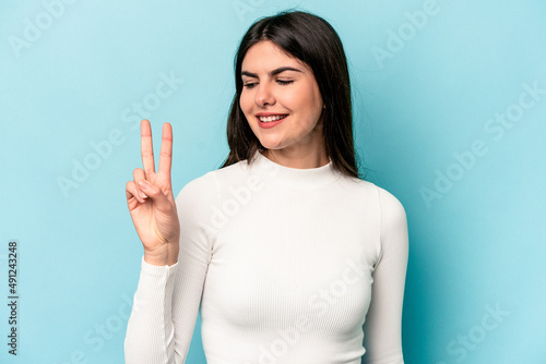 Young caucasian woman isolated on blue background joyful and carefree showing a peace symbol with fingers.